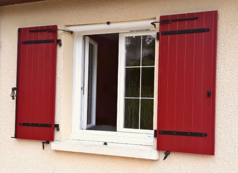 Fenêtre ouverte avec volets battants rouges en composite Yzéa, installés sur une façade claire