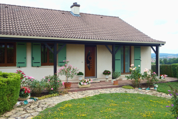 Maison de plain-pied avec volets battants verts en composite Yzéa et jardin fleuri en façade