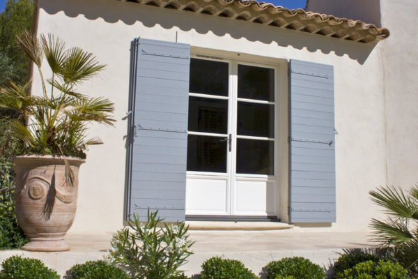 Maison de style méditerranéen avec volets battants gris clair en composite Yzéa installés autour d'une porte-fenêtre blanche
