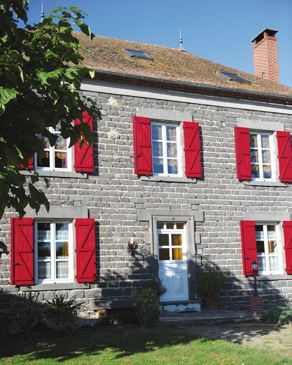 Façade de maison en pierre équipée de volets battants rouges en composite Yzéa
