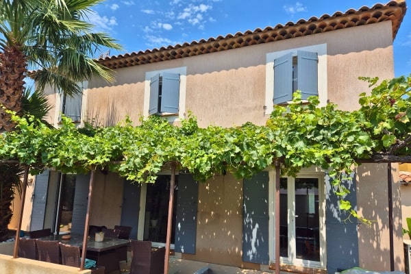 Maison avec volets battants bleu clair et pergola végétalisée, illustrant une installation Yzéa dans un cadre méditerranéen